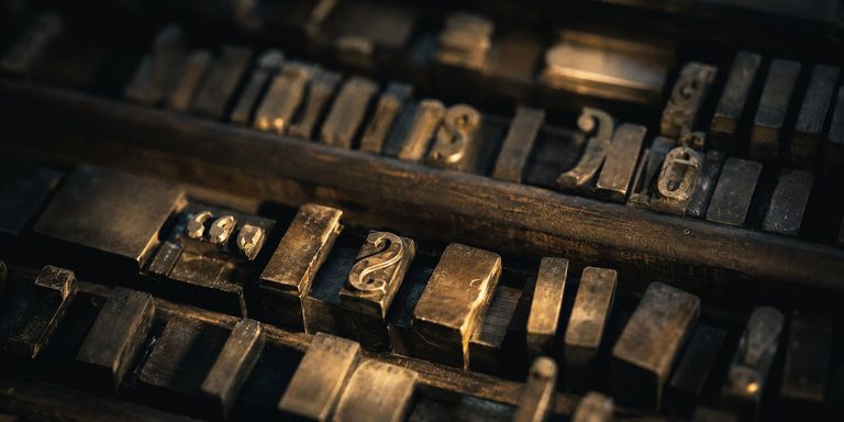 Rows of metal letterpress type sorts resting in a worn wooden case, raked by warm low-angle light.