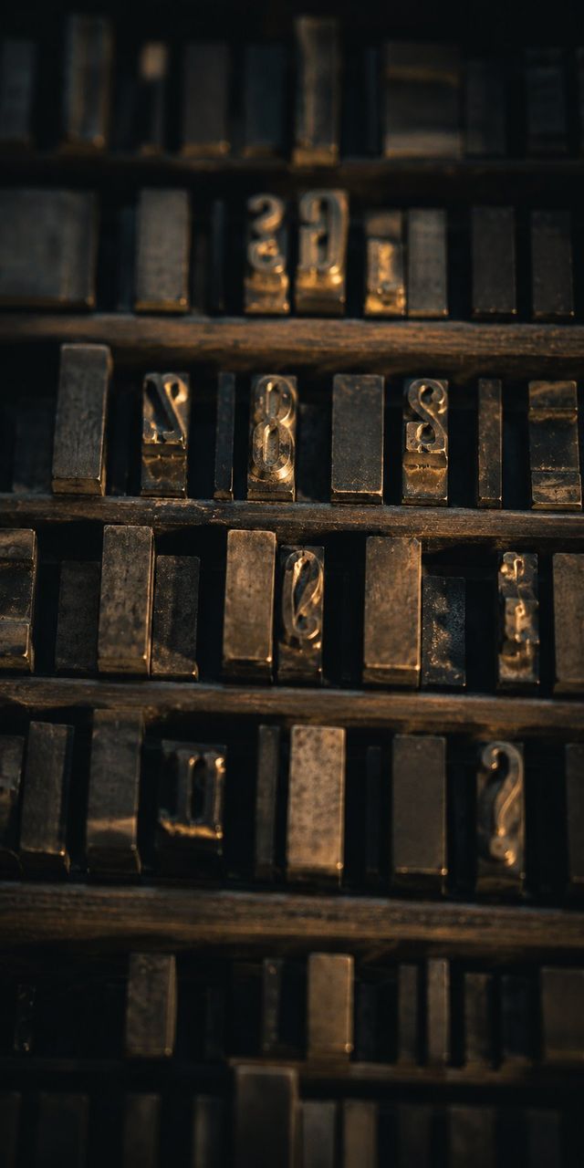 Rows of metal letterpress type sorts resting in a worn wooden case, raked by warm low-angle light.